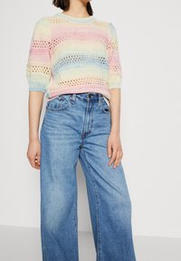 Sweter dzianinowy z pastelowymi poziomymi paskami, kraciastym wykończeniem i krótkimi rękawami, sparowany z szerokimi dżinsami w bladych odcieniach niebieskiego.
