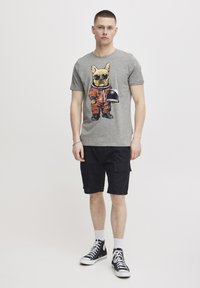 Grå bomull t-skjorte med en hund i oransje astronautdrakt. Kombinert med svarte cargo-shorts og svarte høyde sneakers.