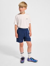 Vit t-shirt med kort ärm och en liten svart logga, marinblå shorts, knähöga vita strumpor med svarta ränder, och flerfärgade träningsskor.