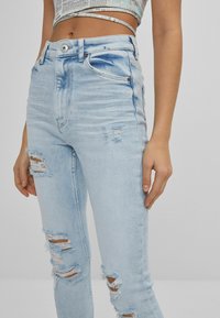 Ljusblå, högmidjade jeans med slitningar, som har en klassisk femfackdesign och en metallknappstängning. Slät denimstruktur.