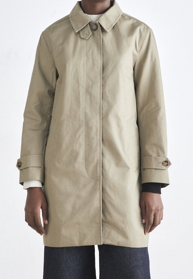 Imperméable kaki avec un col à boutons, des manches longues et des poches latérales. Présente une texture lisse et une légère brillance.