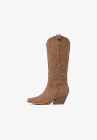 Bota vaquera de gamuza color canela con perforaciones decorativas y costuras, punta afilada y tacón apilado inclinado.