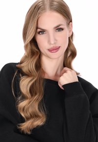 Černá mikina s žebrovanými manžetami, nošená osobou s vlnitými světle hnědými vlasy. Přirozený make-up zvýrazňuje rty a oči.