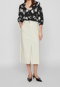 Camicia nera con stampa floreale e maniche a tre quarti, gonna midi crema con spacco frontale e tasche, e décolleté nere a punta con cinturino sul tallone.
