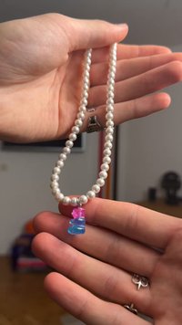 Colar de pérolas brancas com um pendente em forma de ursinho de goma azul e rosa, realçado com ferragens prateadas, exibindo uma textura suave e brilhante.