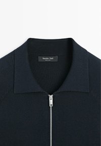 Navy blue zip-up sweater with ribbed texture and a pointed collar. Features a silver zipper and a tag with "Massimo Dutti" label inside.