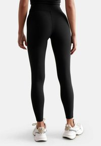 Schwarze hoch taillierte Leggings mit glatter Textur, figurbetontem Schnitt und minimalen Nähten, kombiniert mit hellen Trainingsschuhen.