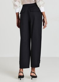 Pantalons larges noirs avec poches arrière, ceinture ajustée et texture lisse. Associés à des talons aiguilles noirs à lanières.