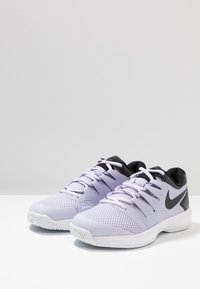 Nike sportovní boty v světlé levandulové barvě s černými akcenty. Síťovina na svršku, kulatá špička, plochá bílá podrážka a šest ok pro šňůrky.