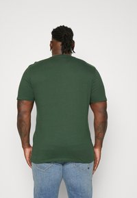Kortermet, mørkegrønn bomulls T-skjorte med rund hals. Glatt tekstur, tettsittende form og minimale designdetaljer. Brukt med lyseblå jeans.