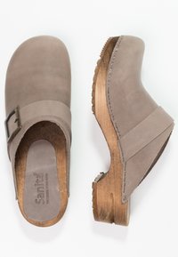 Sabots en cuir gris avec un bout arrondi, une semelle en bois et un détail de boucle. L'intérieur présente une semelle rembourrée pour le confort.