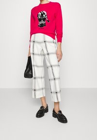 Jasnoróżowy sweter z motywem zebry, zestawiony z białymi, kratkowymi spodniami o długości do kostek. Do tego czarna torebka i masywne czarne mokasyny.