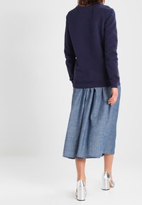 Mörkblå sweatshirt med rund halsringning, kombinerad med en jeanskjol med veck. Silverfärgade platåskor framhäver outfiten.