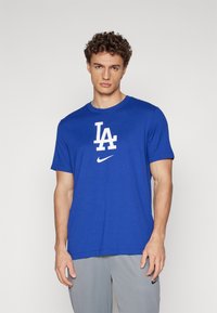 Kék pamut póló kerek nyakkal, fehér "LA" logóval és egy kis Nike swoosh-ral. Rövid ujjú és egyenesen vágott aljjal készült.