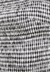 Tissu texturé noir et blanc avec un motif en damier, présentant un design smocké avec des sections froncées tout au long.