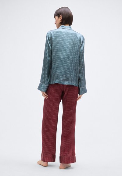 Jedwabny komplet piżamowy z wzorzystą niebieską bluzką z długimi rękawami i bordowymi, wzorzystymi spodniami. Gładka faktura, luźny krój i podwinięte mankiety.