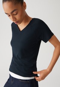Marineblaues, geripptes T-Shirt mit kurzen Ärmeln und V-Ausschnitt; figurbetontes Design mit glatter Textur und einem weißen Innenteil, das am Saum leicht hervorblitzt.