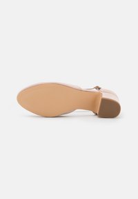 Scarpa con tacco alto in suede rosa, con punta arrotondata, sottile cinturino alla caviglia e suola beige liscia con motivo testurizzato per una migliore aderenza.
