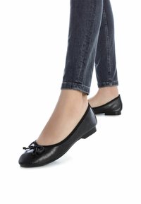 Bailarinas negras hechas de material sintético, con punta redondeada y un pequeño lazo en la parte delantera, y un tacón plano.