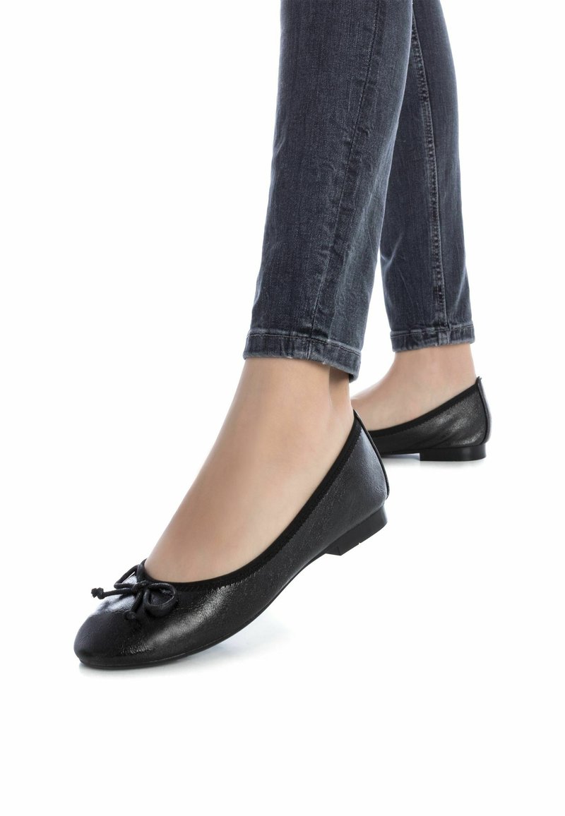 Bailarinas negras hechas de material sintético, con punta redondeada y un pequeño lazo en la parte delantera, y un tacón plano.