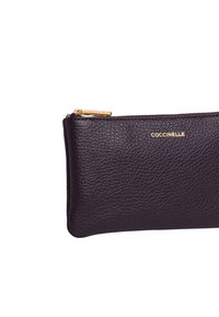 Borsetta zip con texture ciottolata in pelle viola. Caratterizzata da una finitura dorata e una cerniera liscia. Forma compatta e rettangolare.