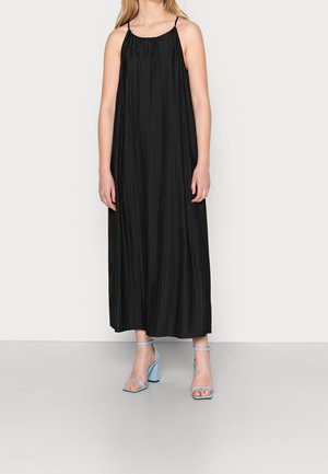 Schwarz plissiertes Maxikleid mit dünnen Trägern und gerafftem Ausschnitt. Kombiniert mit hellblauen Blockabsatzsandalen.