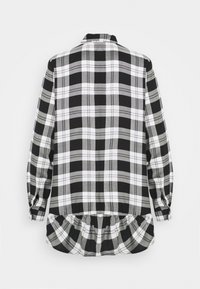 Camicia a scacchi bianca e nera con maniche lunghe, colletto con bottoni e orlo arricciato. Realizzata in tessuto morbido con motivo a scacchi.