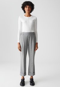 Witte langemouwen top met een ronde hals en een voornaad, gecombineerd met grijze broek met een ruitpatroon, voorzien van een brede tailleband en manchetten.