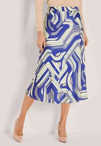Blau- und cremefarbener Rock mit einem fließenden Design, das geometrische Linien zeigt und in mittellanger Länge gehalten ist, kombiniert mit hellen, farbigen Absätzen.