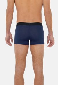 Mörkblå boxerkalsonger i elastisk tyg, med en bred svart midjeband med logotyp, skurna ovanför mitten av låret, slät struktur.