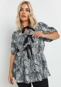 Blusa con estampado de serpiente en blanco y negro, con mangas cortas abullonadas, lazos de tela en el cuello y un dobladillo acampanado. Textura suave, material ligero.