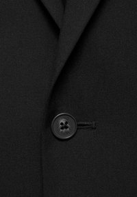 Țesătură de sacou negru cu o textură netedă, având un buton rotund negru cu patru găuri, poziționat pe partea stângă, aproape de rever.