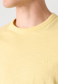 Dzeltena kokvilnas T-kreklu ar apaļu kaklu. Ar smalku, reljefa "BOSS" logotipu saskaņotā tonī uz krūtīm. Gluda tekstūra.