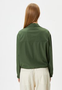 Groene lichtgewicht jas met een kraag, gathers aan de mouwen en een relaxed fit. De achterkant heeft een yoke-detail en een soepele textuur.
