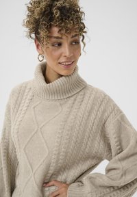 Beiger gestrickter Rollkragenpullover mit einem strukturierten Zopfmuster und weit geschnittenen Ärmeln, ausgestattet mit einem gerippten Kragen und weichem, gemütlichem Stoff.