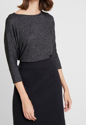 Jupe noire texturée avec un motif subtil, assortie à un haut à manches longues scintillant, sombre, avec un décolleté large et une coupe décontractée.