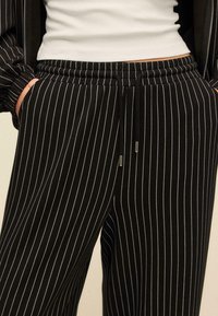 Musta-valkoiset raidalliset housut, joissa on joustava vyötärönauha ja kiristysnyöri. Pehmeä kangas ja rento leikkaus, sivutaskuilla varustettu.
