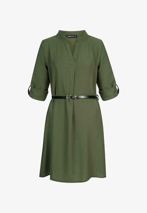 Žalia kelių ilgių suknelė su V formos iškirpte, trijų ketvirčių rankovėmis, sukantys rankogaliai, ir juodas diržas su auksine sagtimi, kad būtų formuojama. Minkšta audinio tekstūra.