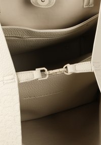 Vitt läderhandväska inuti med en texturerad yta, ett tryckknappslås och en liten ficka med ett metallspänne.