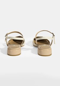 Beige blokhak sandalen met crèmekleurige kruisbanden, een gladde textuur en een verstelbare gesp. Open achterkant ontwerp.