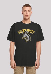 Svart kortermet t-skjorte med et grafisk trykk av et badger og teksten "HUFFLEPUFF" i gult med en slitt tekstur.