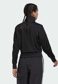 Sudadera negra de cuello alto con mangas largas, tejido texturizado, dobladillo acanalado y rayas laterales, combinada con pantalones oscuros a juego.