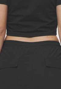 Svart cropped t-skjorte med korte ermer, parret med høyhøstede svarte cargo-bukser med sidelommer og elastisk midje.