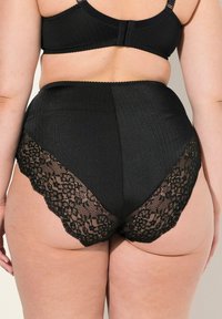 Zwarte high-waisted onderbroek van ribstof met kantafwerking. Heeft een gladde textuur en gegolfde randen langs de kantdetails.