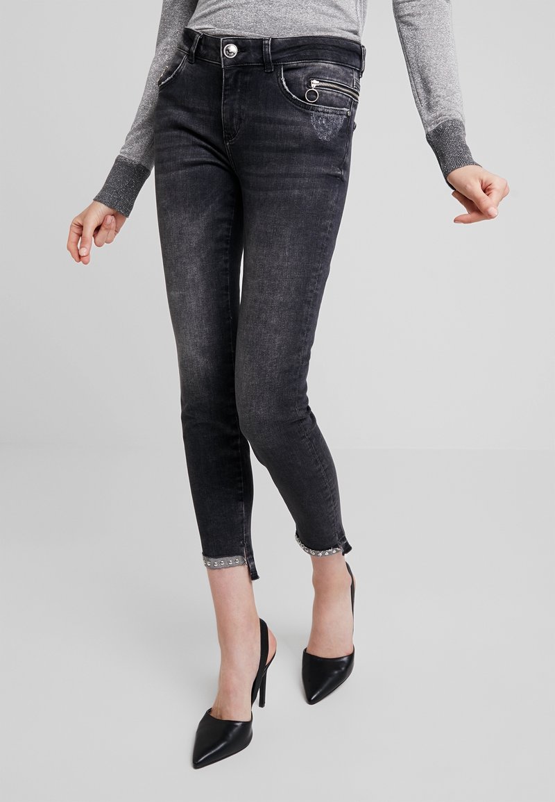 Jean noir ajusté, court, avec détail de bordure cloutée, porté avec un haut gris à manches longues et des escarpins slingbacks noirs à bout pointu.