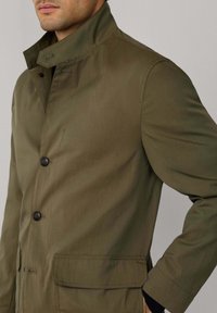 Giacca verde oliva con colletto alto, bottoni frontali e tasche laterali. Realizzata in tessuto texturizzato con vestibilità casual.
