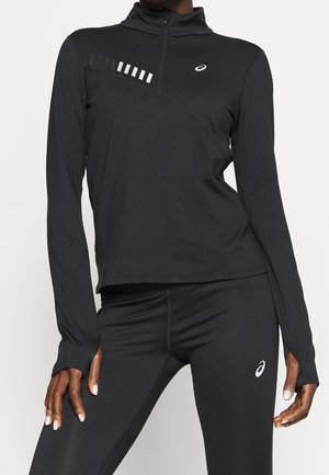 Haut de sport noir à manches longues avec un col zippé mi-hauteur, des bandes réfléchissantes sur la poitrine gauche et une silhouette ajustée.