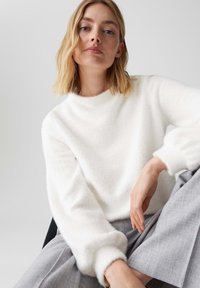 Maglione bianco peloso con collo alto e maniche a sbuffo, abbinato a pantaloni grigi. Tessuto morbido, design semplice, stile minimalista.