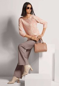 Hellrosa gemusterter Pullover, beiges High-Heel-Schuhwerk, taupe-farbene weite Hose und eine geflochtene Blush-Handtasche. Die Accessoires umfassen Sonnenbrillen und Armbänder.