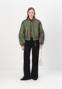 Olivgrön bomberjacka med dragkedja fram, ribbade ärmslut och midja. Kombineras med svarta utsvängda jeans och en liten handväska i krämfärg.